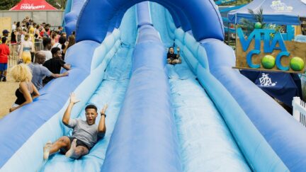 LONDON, ENGLAND - JULY 22: Festival goers slide down Vita Coco's Slip N' Slide during Lambeth Country Show at Brockwell Park on July 22, 2018 in London, England. Vita Coco bought the UK's largest inflatable water slide to the Lambeth Country Show in a bid to help Londoners cool down during one of the hottest summers on record in the UK. (Photo by Tristan Fewings/Getty Images for Vita Coco)