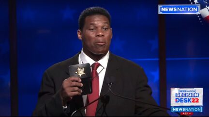 Herschel Walker holds up badge prop