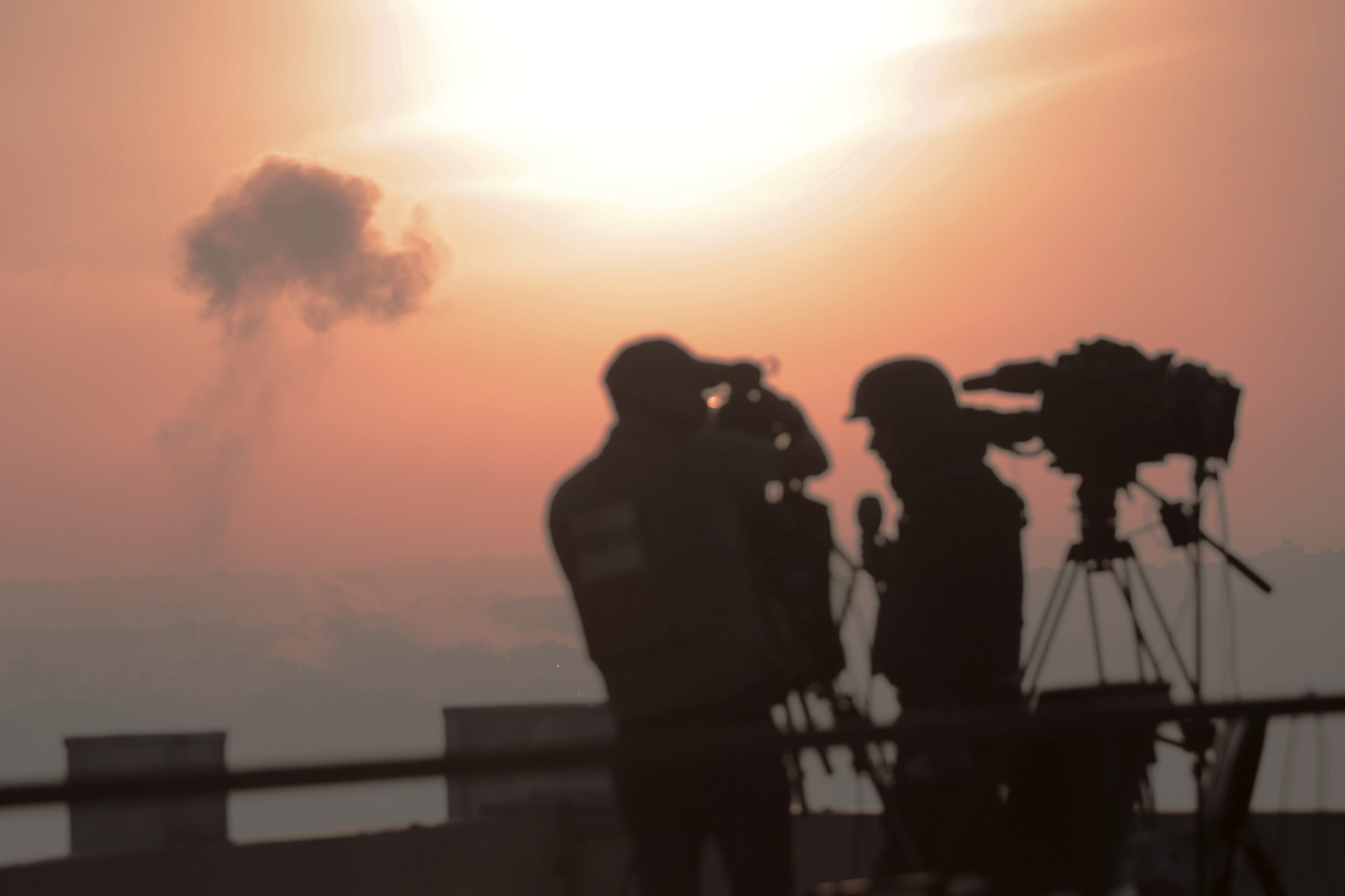 Palestinian journalists are working with an image of an Israeli airstrike in the background.