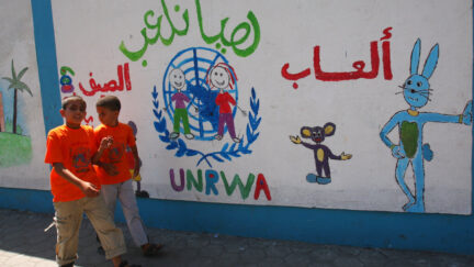Palestinian youths walk next to a wall of a school run by the UN Relief and Works Agency, (UNRWA), decorated with graffiti painted by the school children as a part of summer activities in Gaza City, Tuesday, July 28, 2009. Some 280 schools were damaged and 18 destroyed in Israel's three-week offensive against Gaza's Hamas rulers seven months ago.