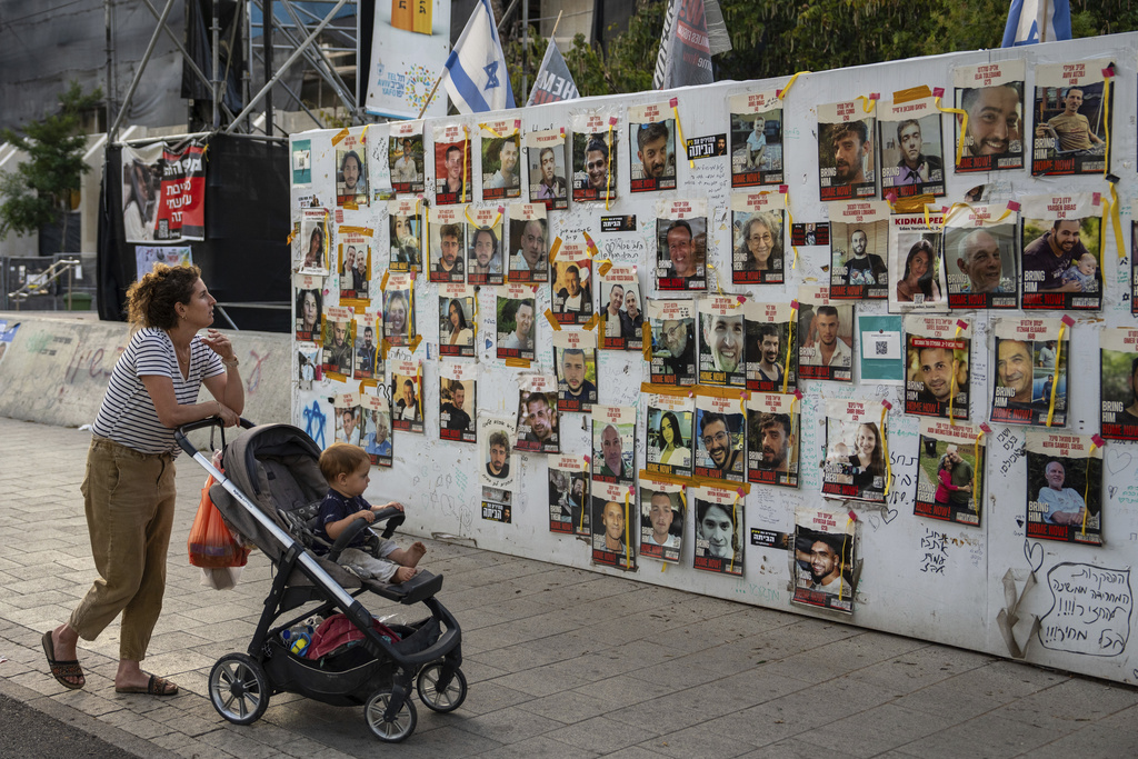 Passersby observe the photos of hostages held in the Gaza Strip that are plastered to the walls of a plaza known as Hostages Square in Tel Aviv, Israel, Friday, May 17, 2024. The Israeli military said Friday its forces rescued from Gaza the remains of three Israeli hostages taken by militants during the Oct. 7 attack, including 22-year-old German-Israeli Shani Louk, 28-year-old Amit Buskila, and 56-year-old Itzhak Gelerenter.