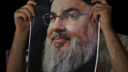 A man covers his by a portrait of Hezbollah leader Sayyed Hassan Nasrallah during a protest in the southern port city of Sidon, Lebanon, Saturday, Sept. 28, 2024.