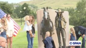 Kristi Noem holding a young child next to the bronze statue of her and a horse