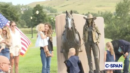 Kristi Noem holding a young child next to the bronze statue of her and a horse
